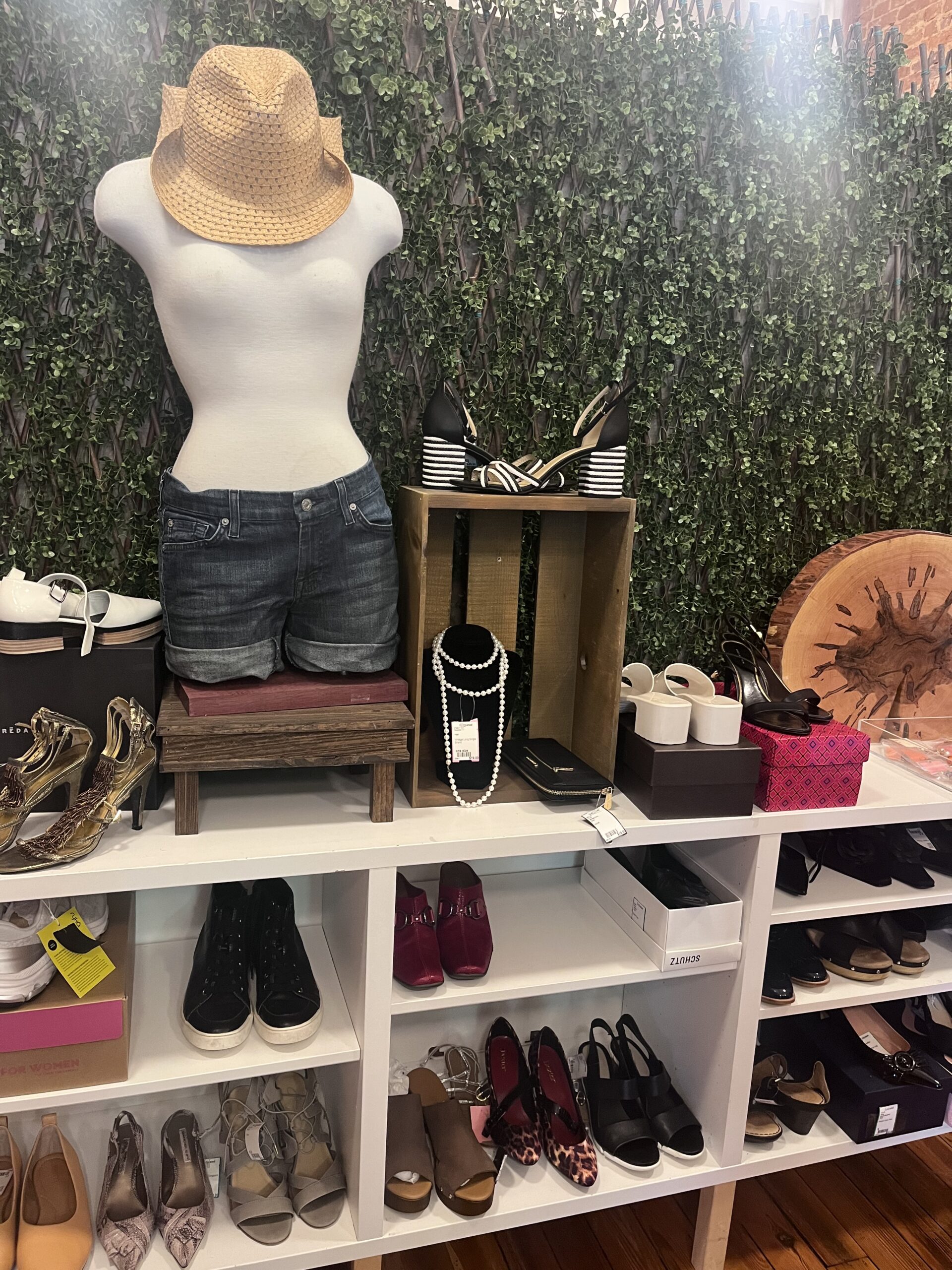 Mannequin with hat and shirt and shorts, on shelf with shoes and boots on it.